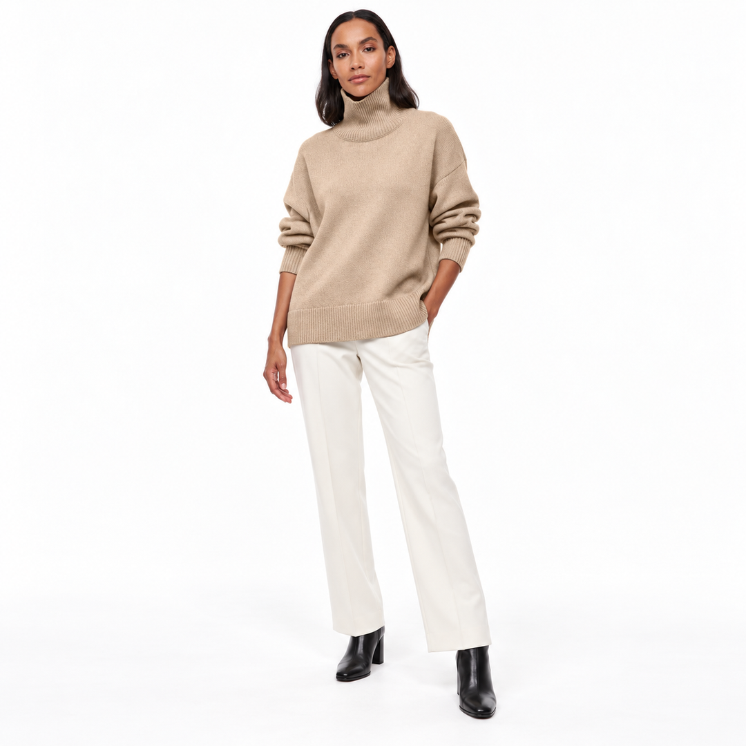 Full-length model wearing a light khaki ribbed-trim turtleneck sweater with ivory tailored trousers and black boots on white.