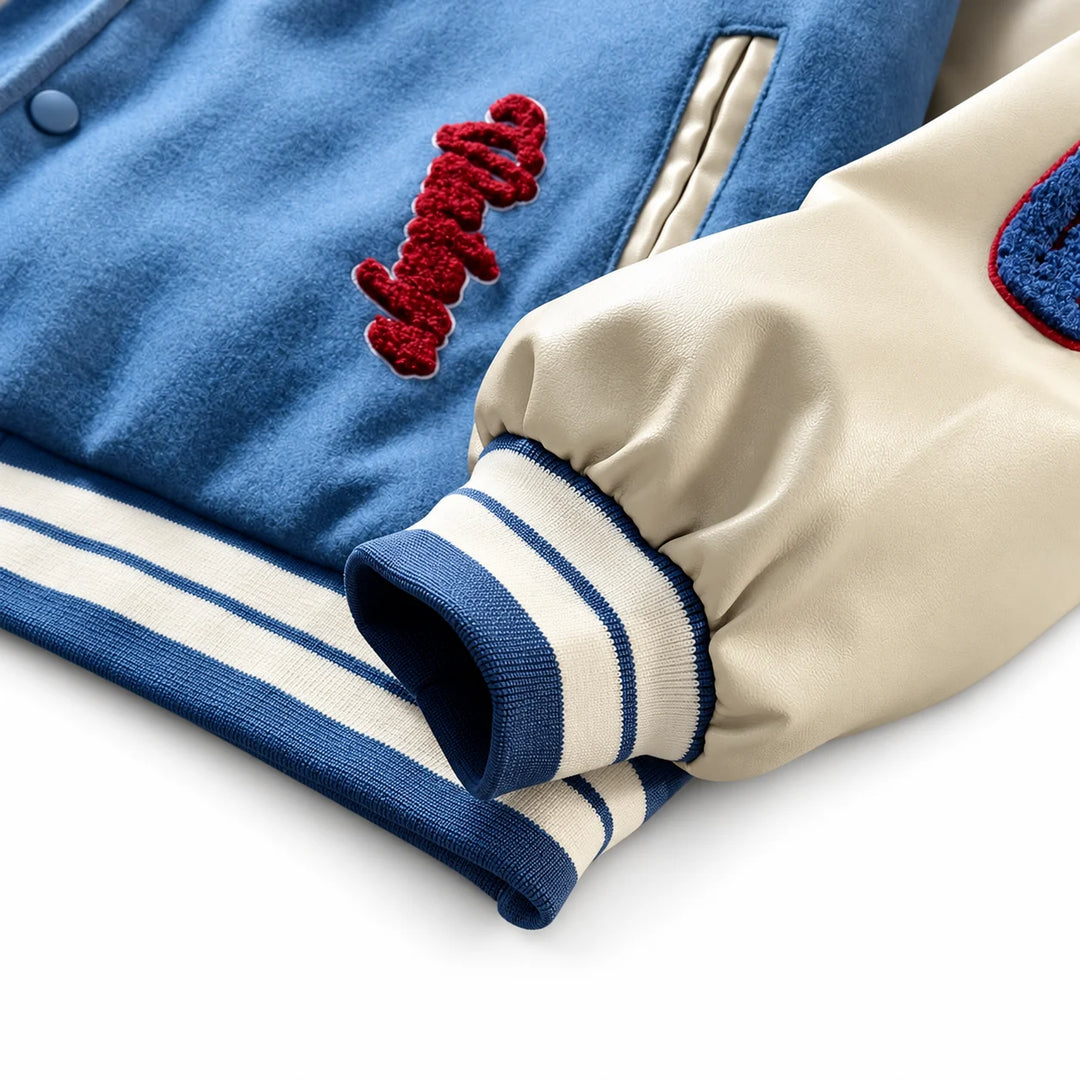 Blue varsity jacket detail showing a cream sleeve, striped ribbed cuff and hem, contrast pocket trim and red embroidery.