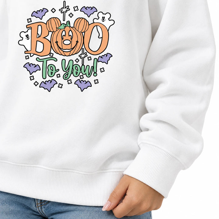 White sweatshirt detail with a ribbed sleeve cuff, ribbed hem and fabric folds beside jeans on a model on a white background.