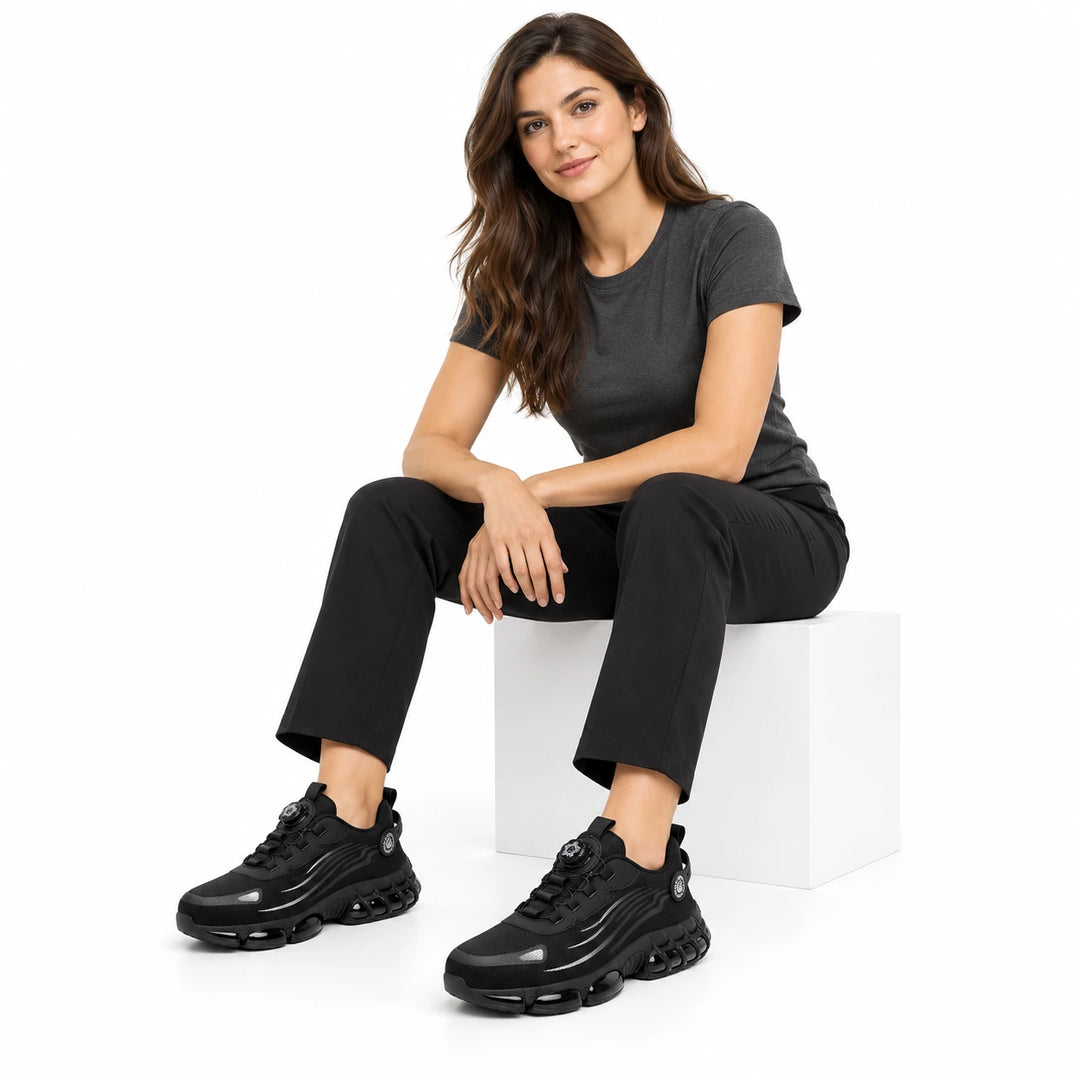 Female model wearing black athletic steel toe shoes with silver accents and black trousers.