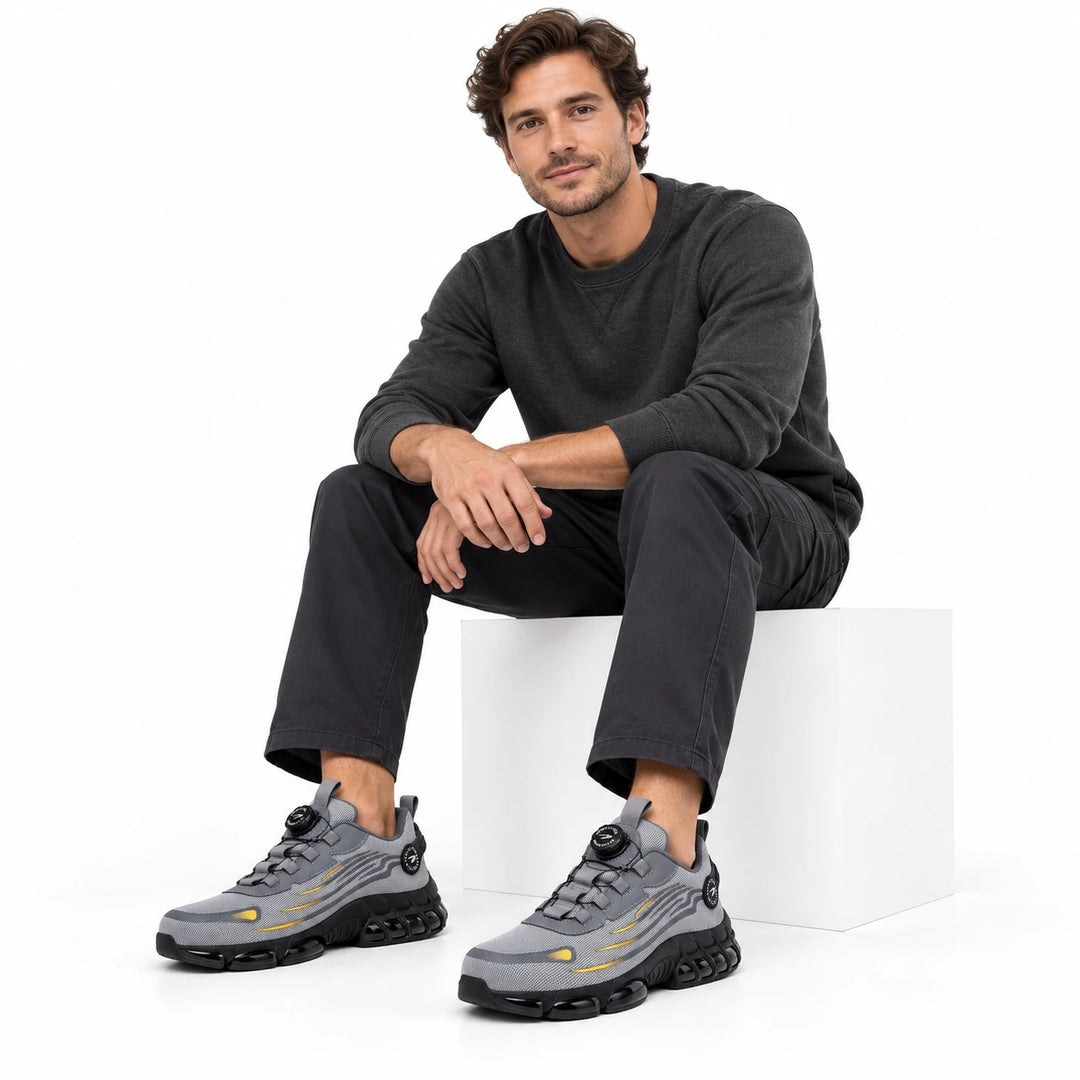 Male model wearing grey athletic steel toe shoes with dark work trousers in a white studio.