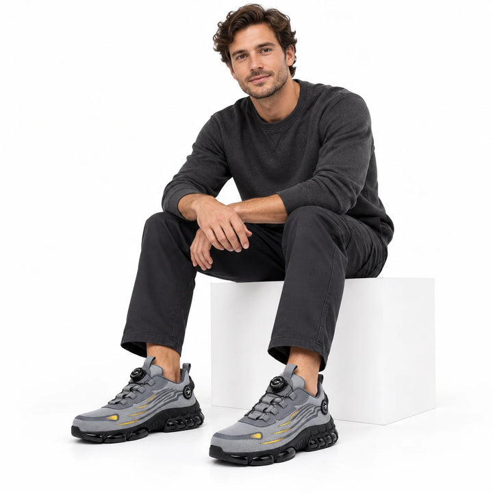 Male model wearing grey athletic steel toe shoes with dark work trousers in a white studio.