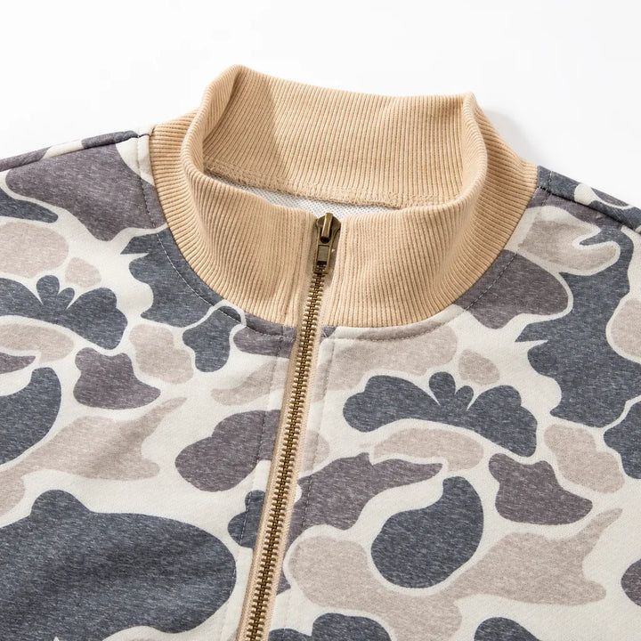 Close-up of the beige ribbed bomber collar, closed gold-tone zipper and cream, charcoal and taupe camouflage fabric on white.