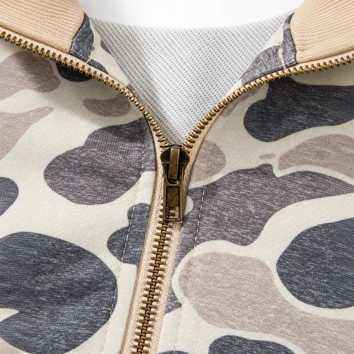 Close-up of a gold-tone zipper slider and teeth, with neckline stitching, interior fabric and camouflage print clearly shown.