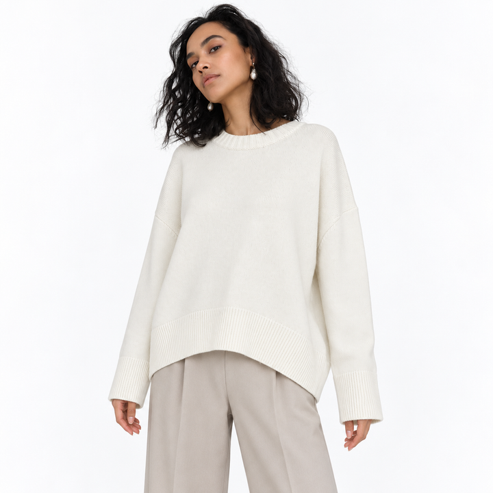 White knitted pullover on a model in a white studio, showing its crew neckline, long sleeves, relaxed shape and ribbed edges.