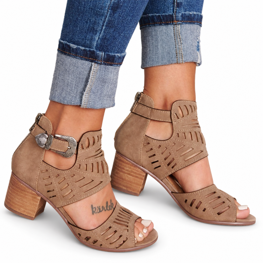 Brown cutout sandals with side buckles, open toes and separate broad heels, worn with cuffed jeans against a white background