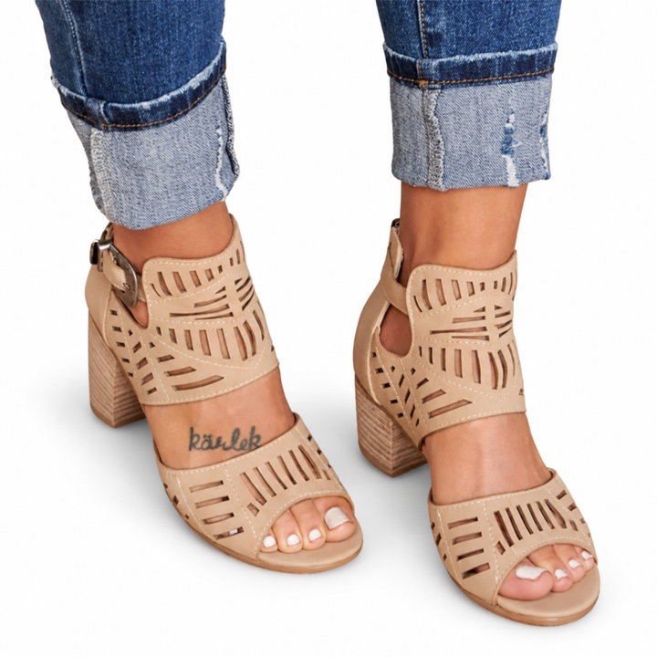Khaki cutout sandals viewed from the front, showing open toes, ankle buckles and broad heels against a white studio backdrop.