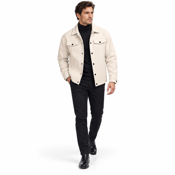 Apricot jacket styled over a black turtleneck on an adult male model walking in a white studio with black trousers and boots.