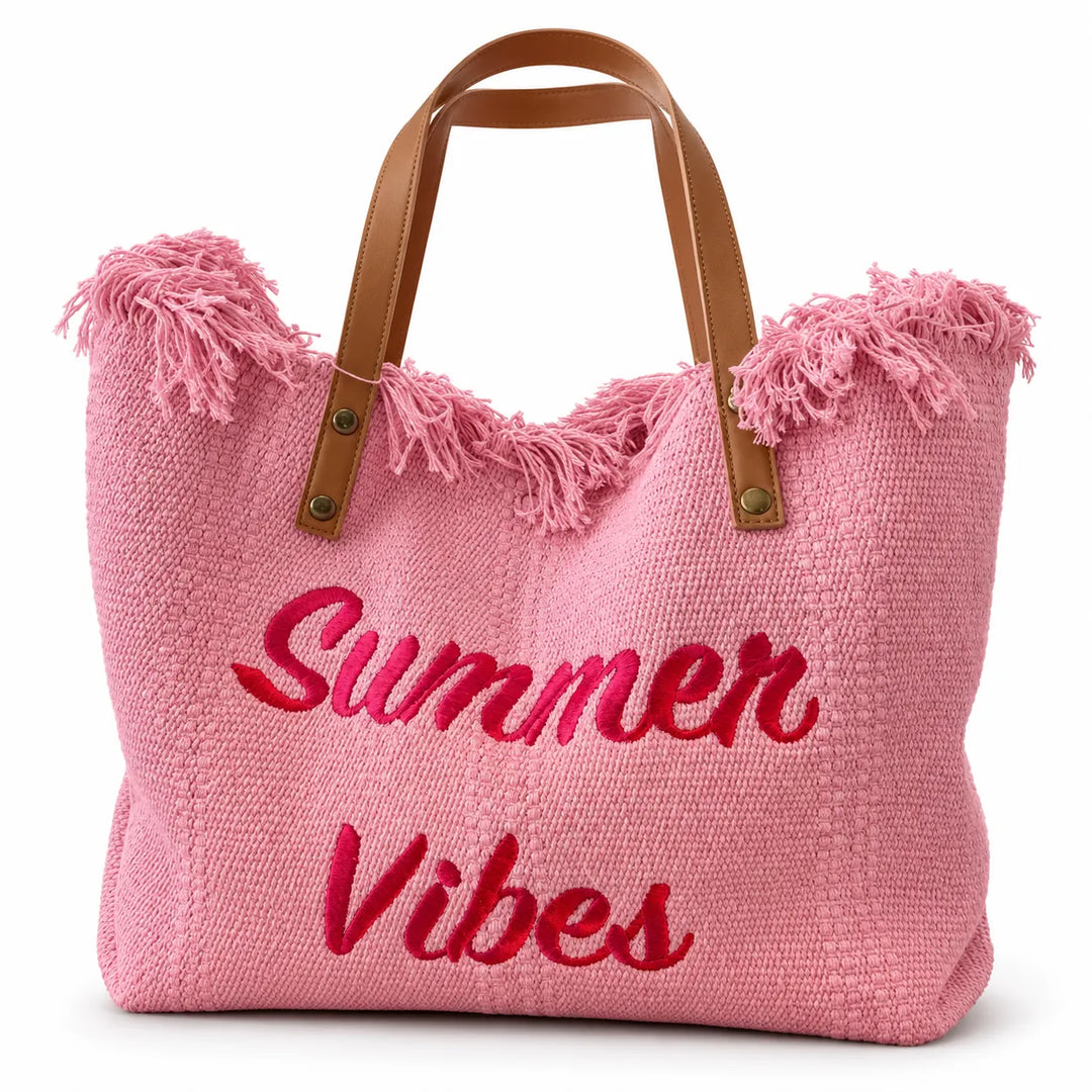 Pink tote bag with magnetic closure, brown handles, a fringed top and red Summer Vibes lettering on a white studio background