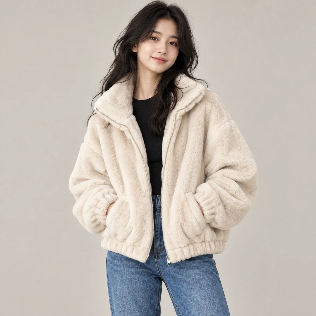 Model wearing the beige plush jacket with a black top and blue jeans, showing the collar, zipper and front pockets in studio.