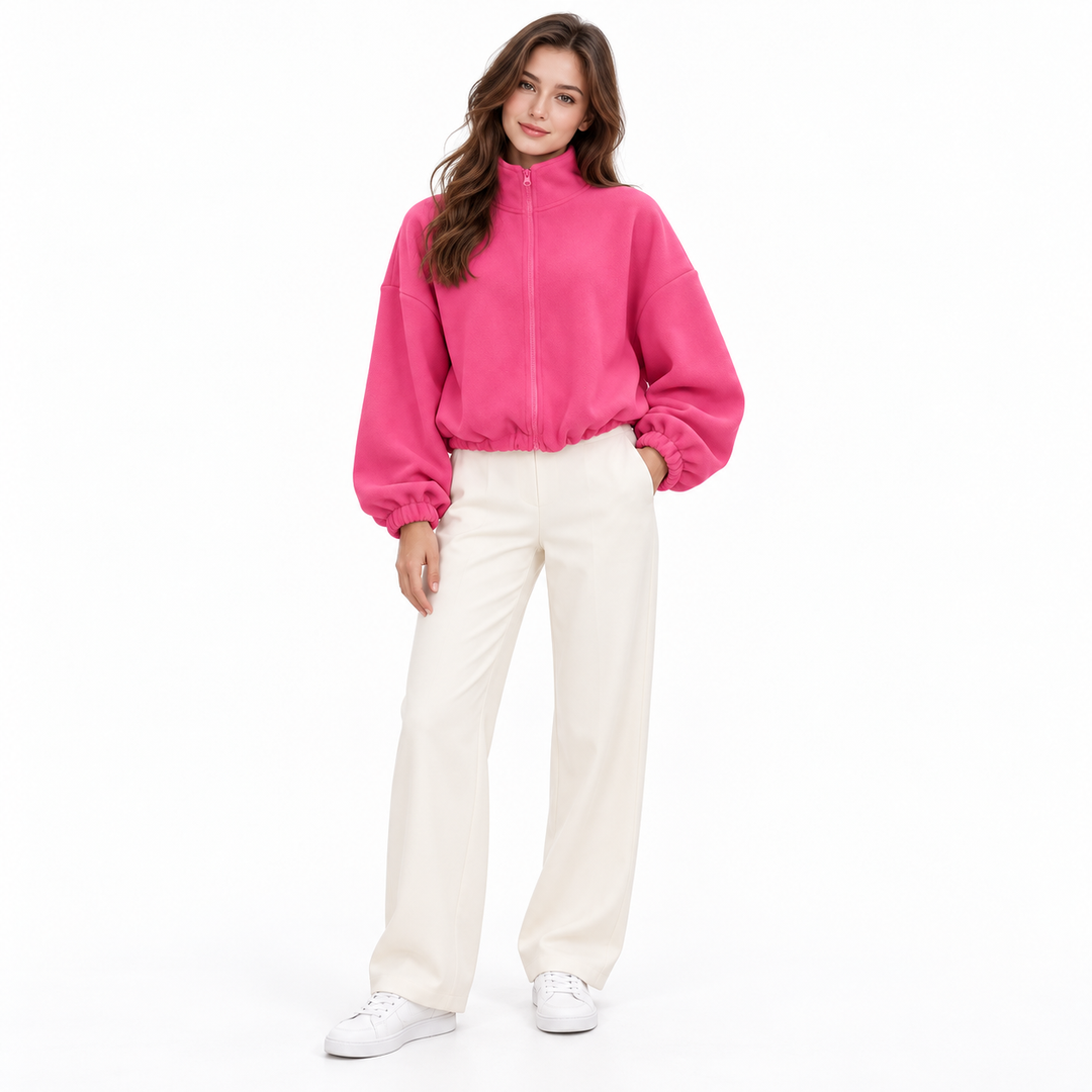 Rose pink cropped jacket on a full-body brunette model showing its stand collar, zipper and gathered hem with ivory trousers.