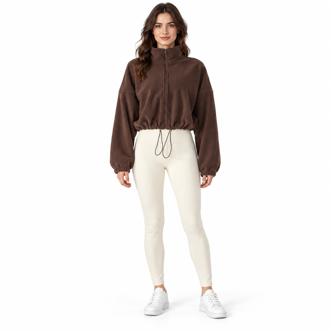 Dark brown cropped jacket on a full-body brunette model with a stand collar, zipper and drawcord, styled with ivory trousers.