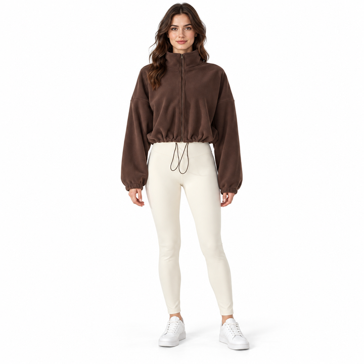 Dark brown cropped jacket on a full-body brunette model with a stand collar, zipper and drawcord, styled with ivory trousers.