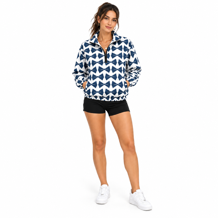 Adult woman wearing navy and white geometric half zip jacket with black shorts and white sneakers on a white studio backdrop.