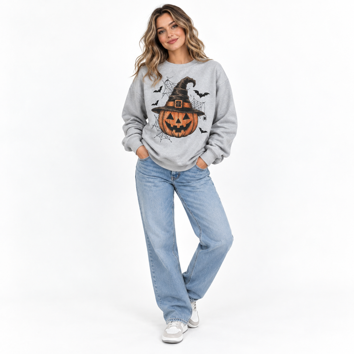 Model wearing Halloween sweatshirt with pumpkin, witch hat, bats and spider web graphic in the bright studio product setting.
