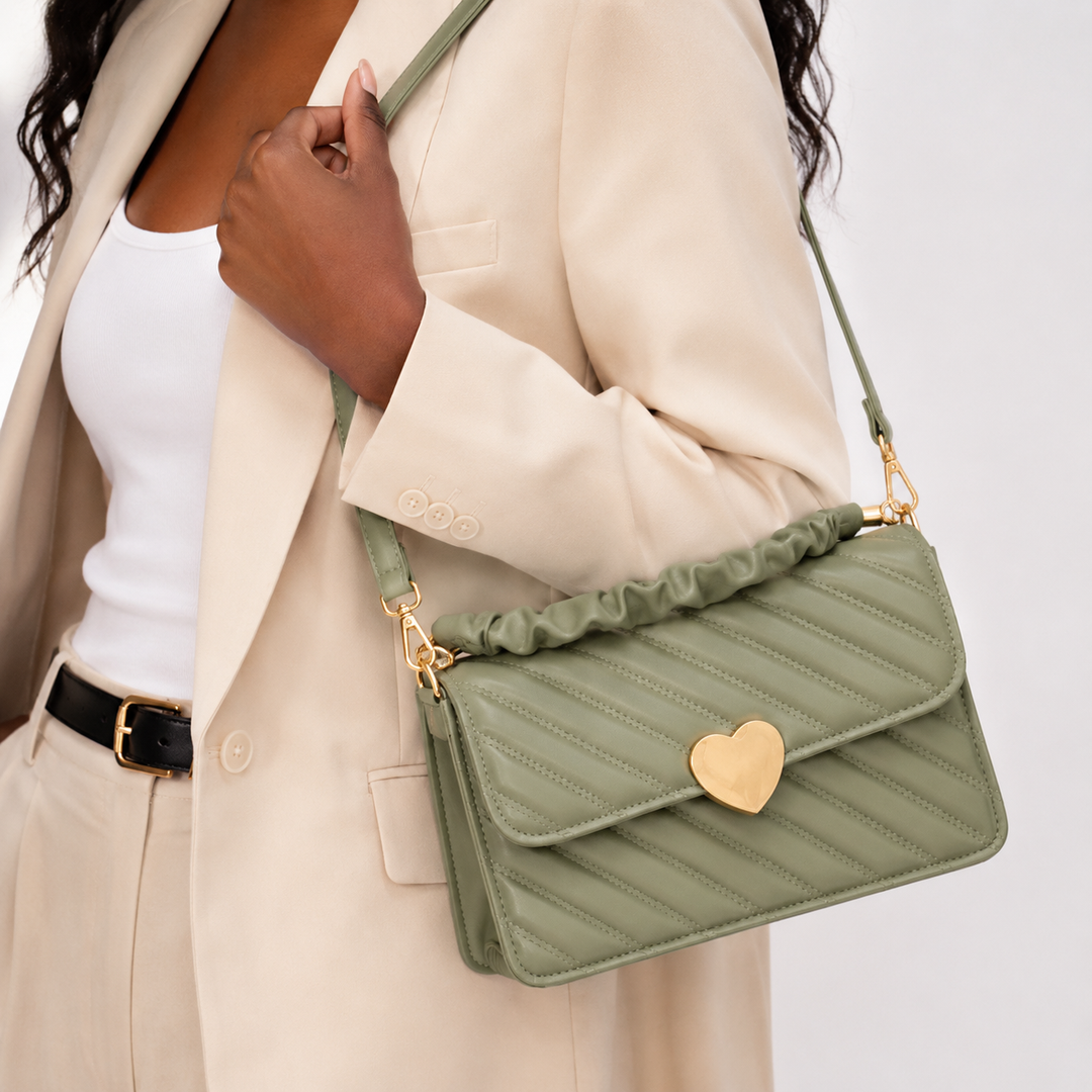 Close-up of the sage green quilted shoulder bag showing diagonal stitching, ruched handle, gold hardware and heart clasp.