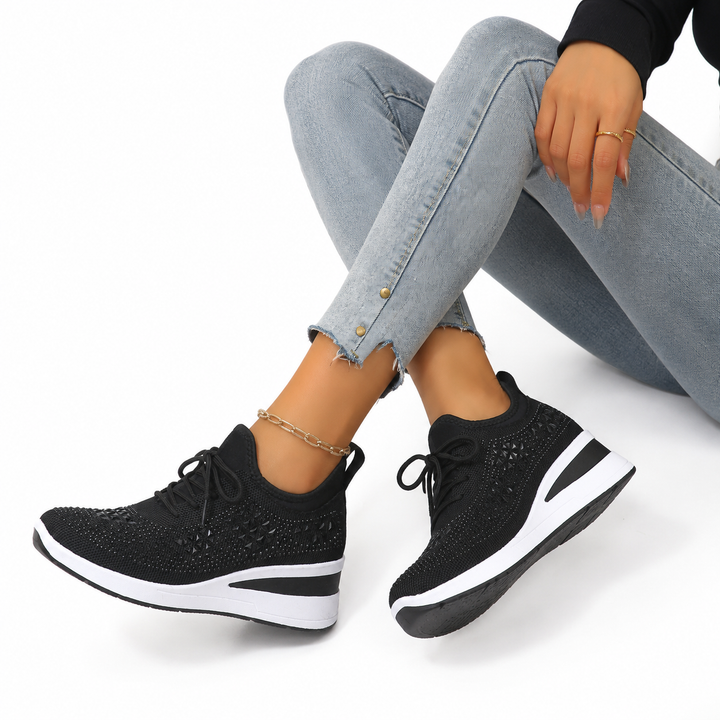 Black rhinestone wedge sneakers on a woman against a clean white studio background.