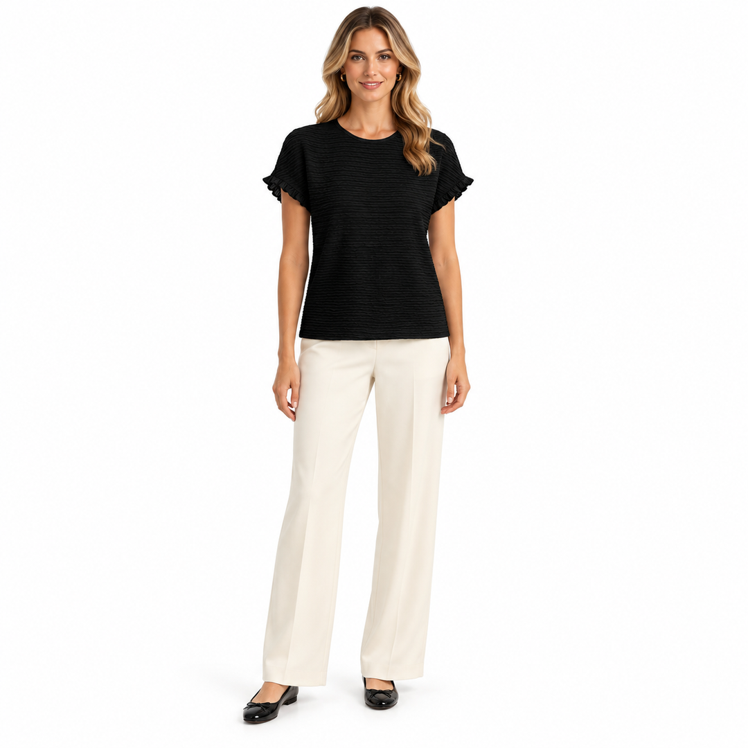 Black short sleeve top on a full-length model with cream trousers, showing a round neckline, ruffled edges and textured front