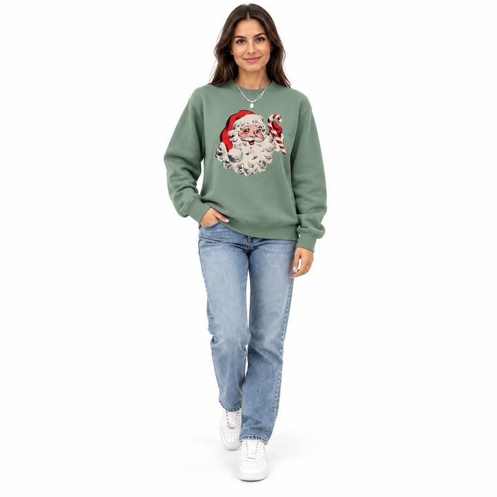Full-length woman wearing an olive green crewneck with Santa Claus &amp; candy cane print, jeans and sneakers on a white backdrop