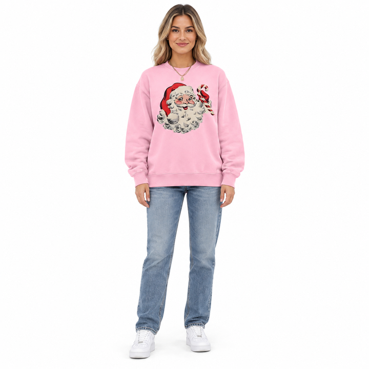 Front view: a woman wearing a pink crewneck with Santa Claus &amp; candy cane print, jeans and sneakers against a white backdrop.