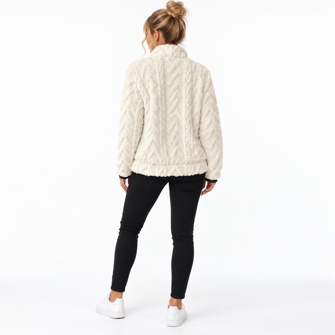Back view of the white textured pullover on a blonde model with tied-up hair, black trousers and white shoes on studio floor.