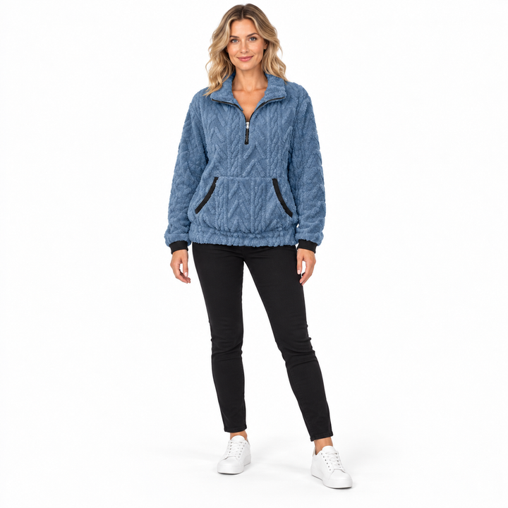 Blue textured zip-neck pullover on a full-body blonde model in black trousers and white sneakers, showing front pocket trims.