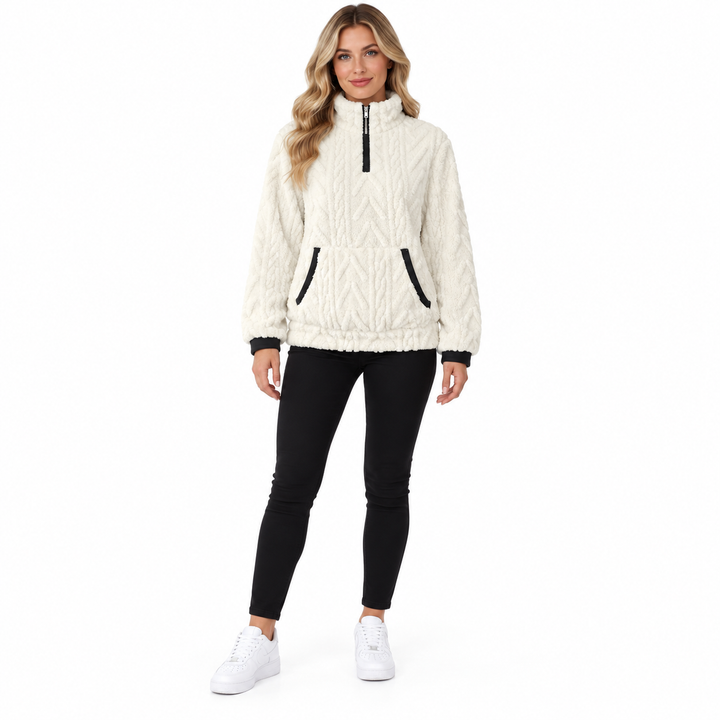 Front view of the white textured pullover on a blonde woman with closed zip collar, black cuffs, black trousers and sneakers.
