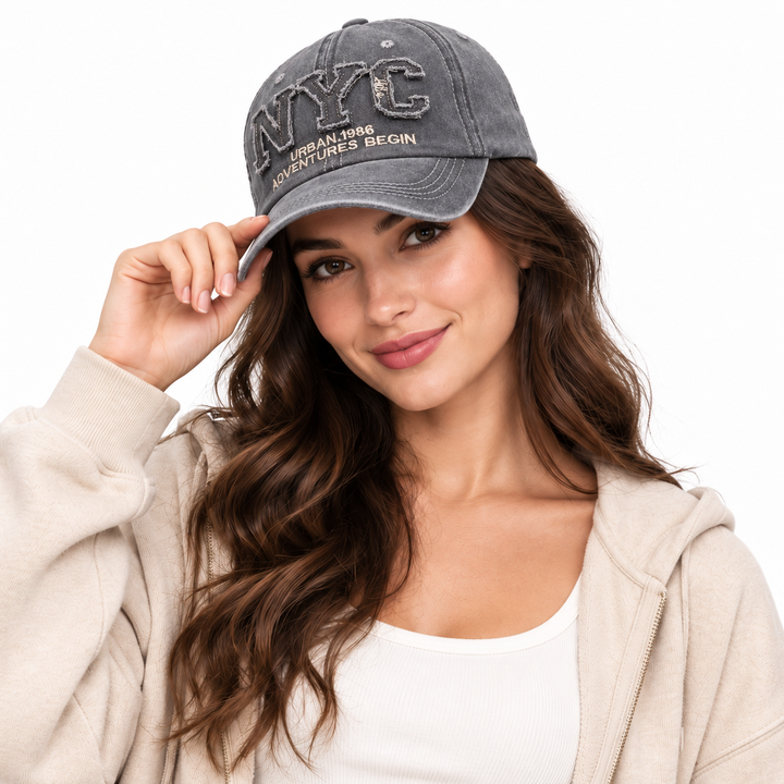 Woman wearing the gray adjustable NYC baseball cap with curved brim and embroidered front in a clean white studio setting.