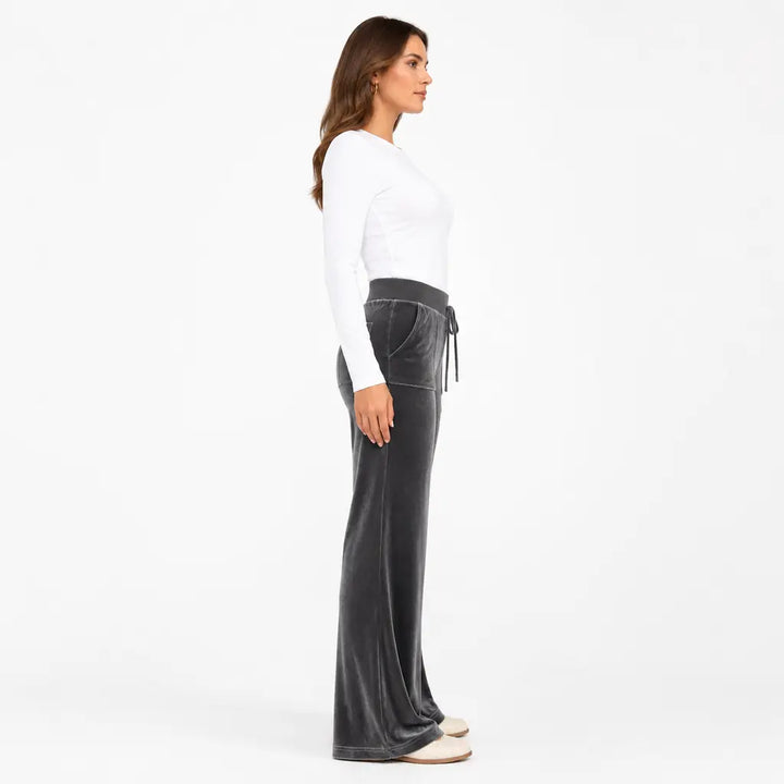 Side profile of dark gray velvet flare pants on a model showing high waist, front pocket placement and flared leg silhouette.