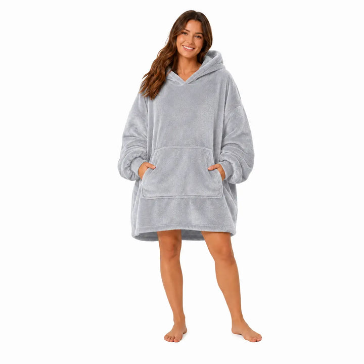 Gray wearable blanket hoodie with hood and large front pocket modeled by a woman on a clean white studio background.