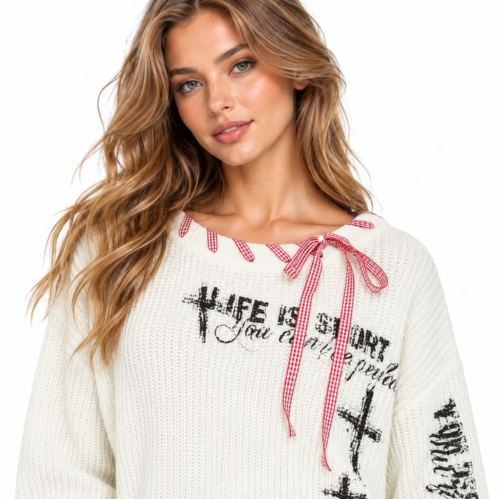 White knit sweater close-up showing black graphic print and red gingham lace-up detail