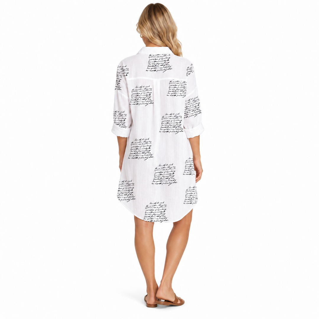 Back view of white shirt dress with black script print, rolled sleeves and curved hem, shown full length on a studio model