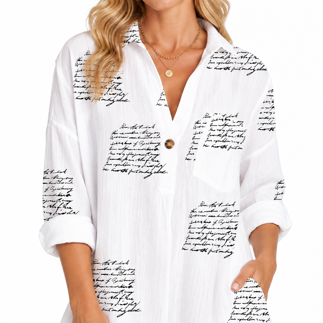 Close-up of collar, V-neck opening, button placket, rolled sleeve and black script print on the white shirt dress fabric