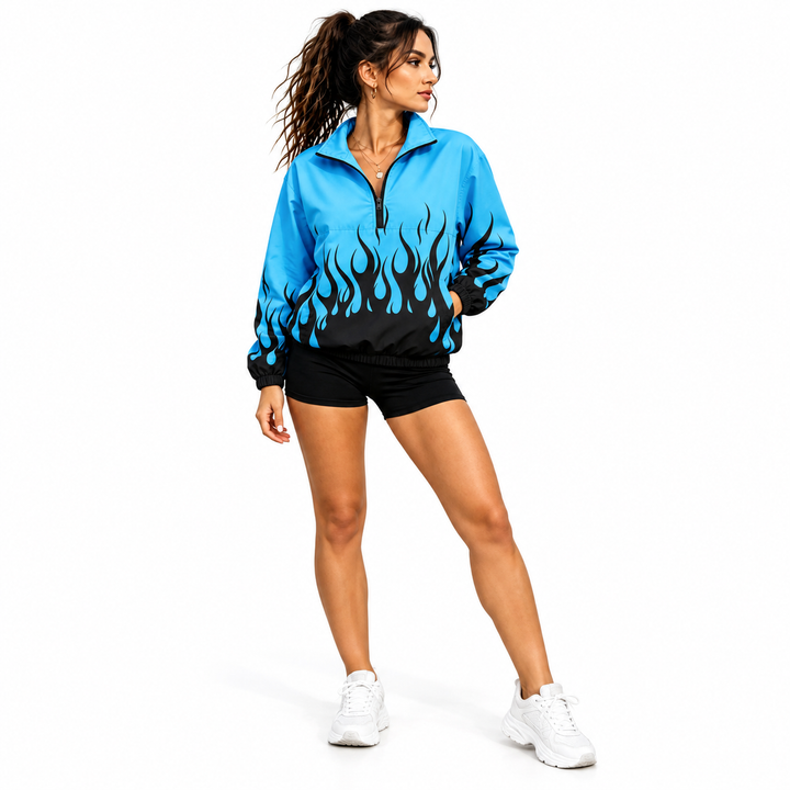 Side-angled view of a woman wearing a blue and dark flame pullover jacket, black shorts and white sneakers in a white studio.