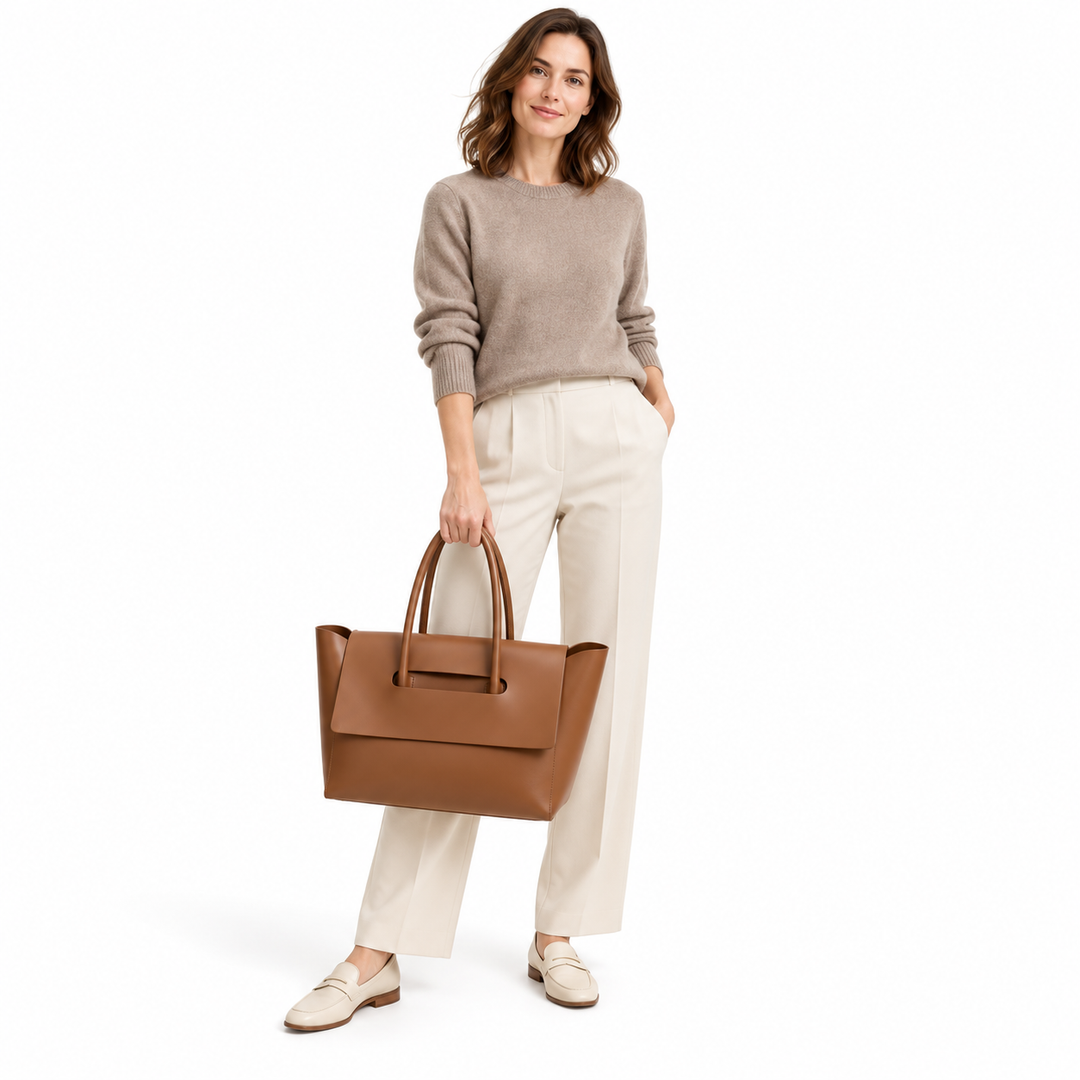 Adult woman in a taupe knit and cream trousers holds the Brown tote, with her outfit visible against a white studio backdrop.