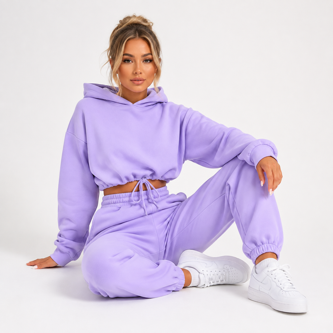 Women tracksuit set in purple on a female model with cropped hoodie, matching joggers and sneakers on a clean white backdrop.