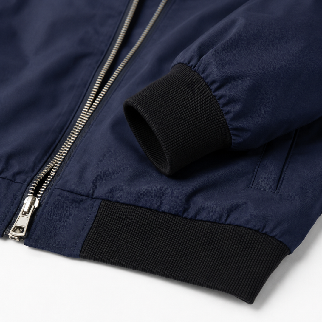 Navy bomber jacket close-up showing smooth fabric, silver front zip, stitched seams, black ribbed cuff and ribbed hem detail.