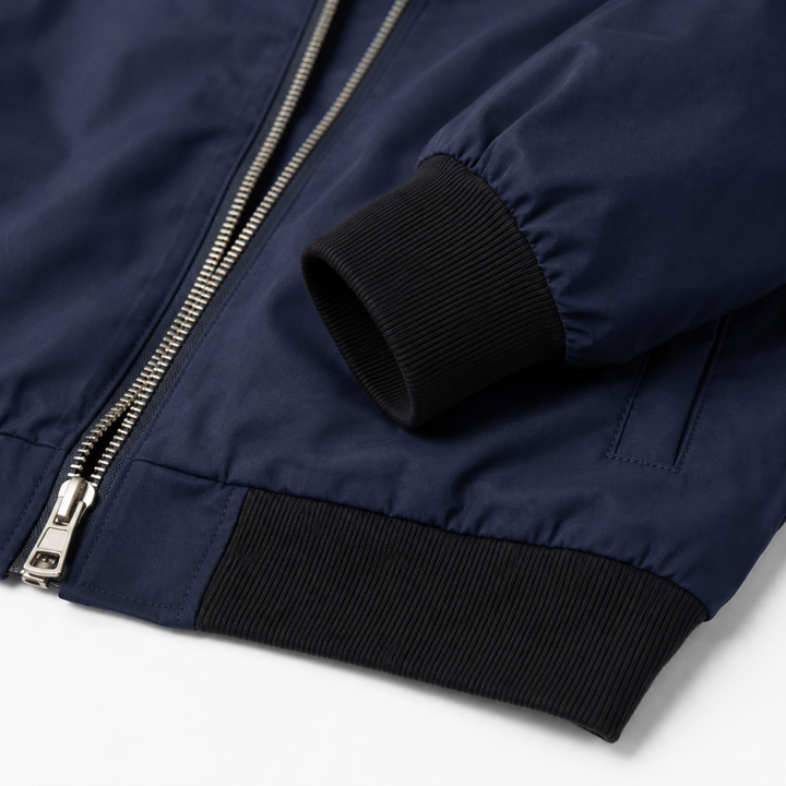 Navy bomber jacket close-up showing smooth fabric, silver front zip, stitched seams, black ribbed cuff and ribbed hem detail.