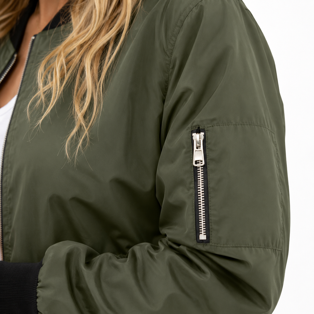 Olive bomber sleeve close-up showing upper-arm zip pocket, silver hardware, clean seam detail and a black ribbed cuff finish.