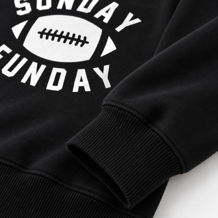 Close-up of black football graphic sweatshirt showing ribbed cuff, hem seam, texture and Sunday Funday print detail up close.