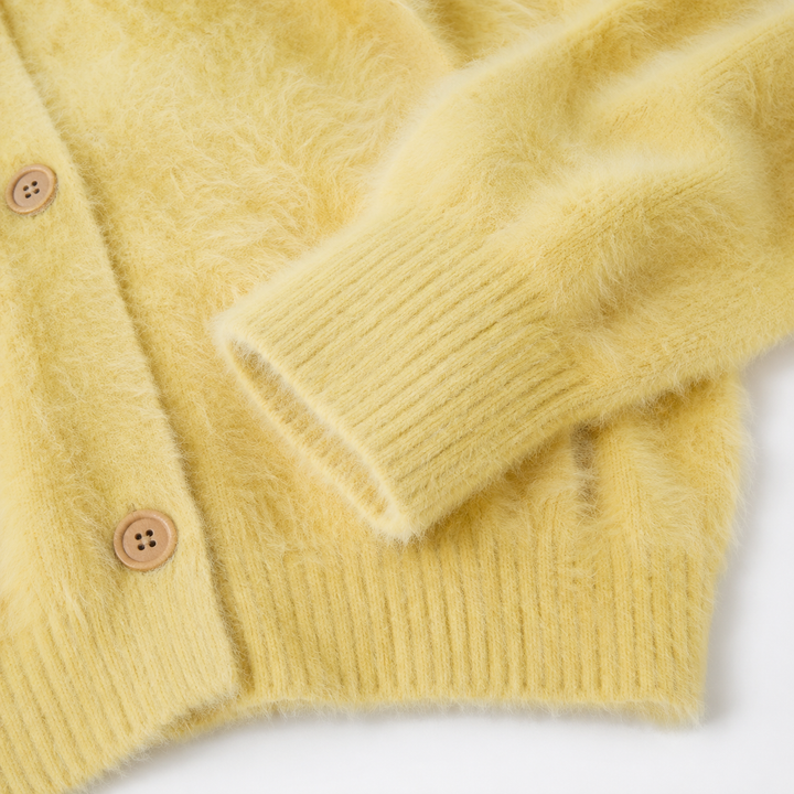 Close-up of the pale yellow cardigan showing fuzzy knit texture, ribbed cuff, ribbed hem and front buttons on a clean background.