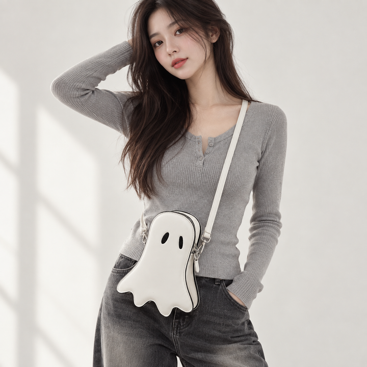 White ghost crossbody bag worn by a model with black oval eyes, contrast piping, zipper and long shoulder strap
