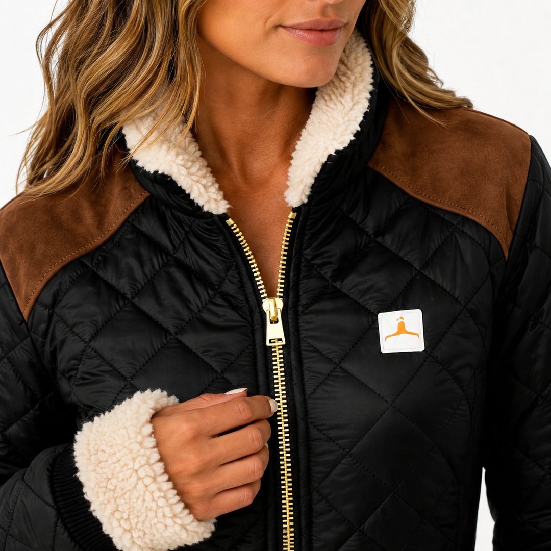 Detail view of quilted jacket collar and zipper, cream cuff trim, brown shoulder panels and small chest patch on black fabric