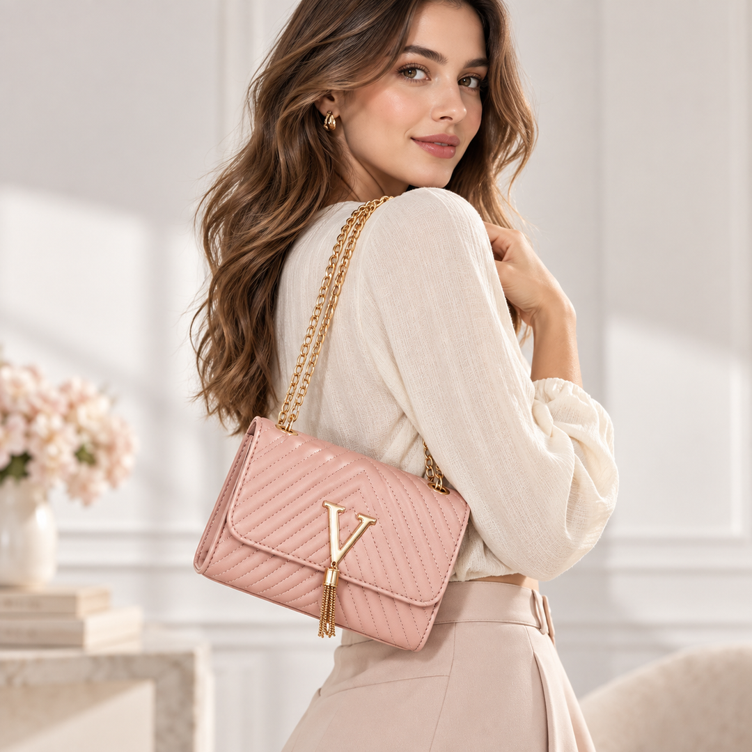 Woman wearing the pink quilted shoulder bag with gold chain strap, V clasp and tassel in a soft neutral fashion setting.