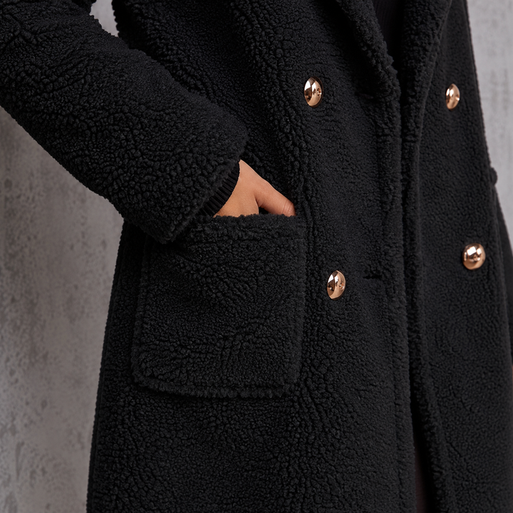 Black teddy coat detail showing patch pocket, plush texture, double-breasted buttons, and clearly visible stitched finishing.