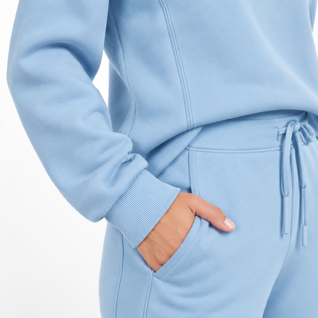 Sky blue tracksuit close-up showing visible seams, cuff, trouser pocket and drawstring waist detail on a clean studio background