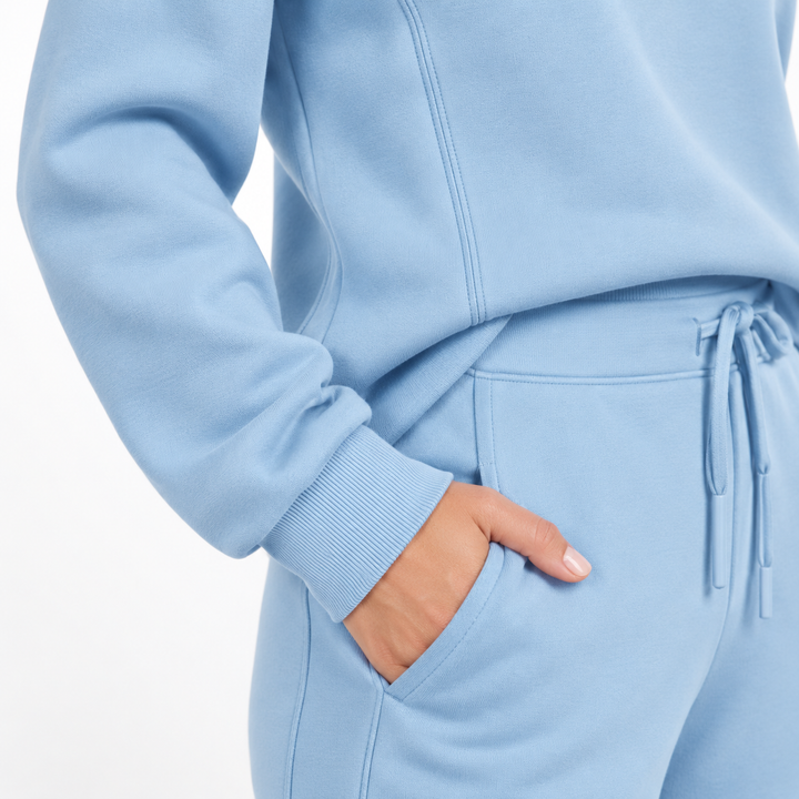 Sky blue tracksuit close-up showing visible seams, cuff, trouser pocket and drawstring waist detail on a clean studio background
