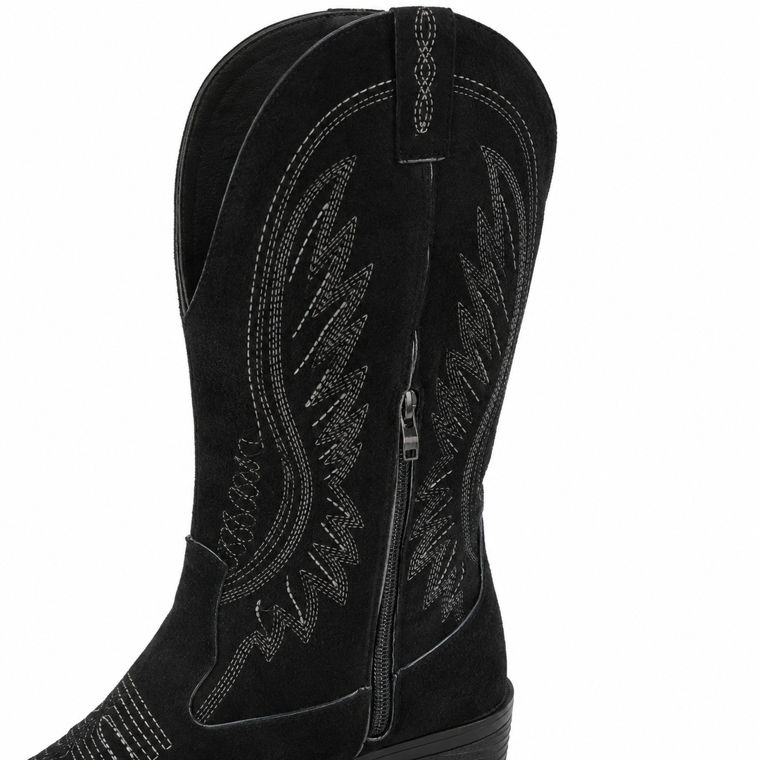 Black suede boot close-up showing the V-cut shaft, fine western embroidery, side zipper and visible surface texture on white.