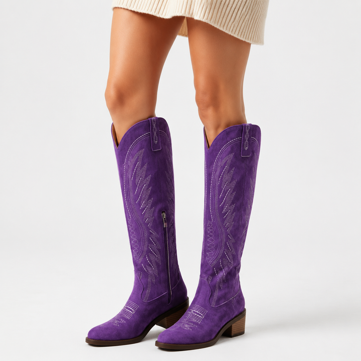 Adult woman wearing Purple V-cut suede boots with western embroidery, side zippers and stacked heels in a clean white studio.