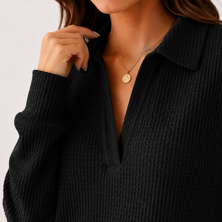 Black collared long sleeve top close-up showing waffle texture, V-neck placket, sleeve cuff and clean seam detail on a model.